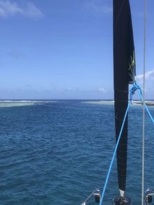 view from the front of the boat with the foresail visible rolled up and a pass of water with almost drying reef on either side