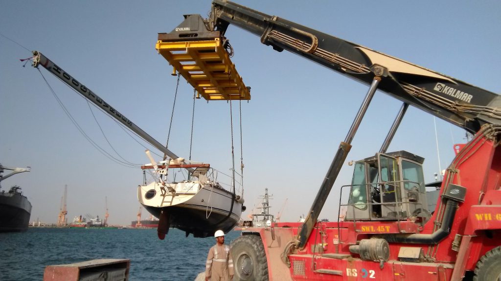 a red crane with a big cab on top lifting a boat out of the water using strops