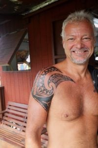man with no shirt on sporting a black polynesian tatoo across his upper arm and right shoulder