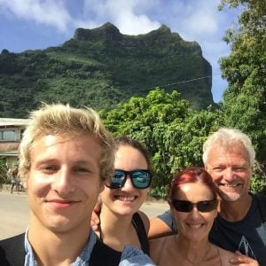 family of four with the son about eighteen in the front taking the selfie with blond short hair, then the daughter perhaps a little older with sunglasses and dark long hair, then mum with red hair and sunglasses and much shorter then Dad with short white hair and the mountains of moorea behind
