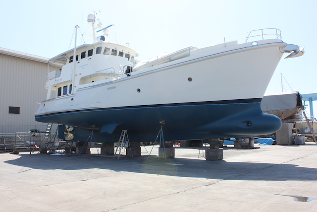 large white motoryacht with white hull and superstructure and blue keel up on blocks in a boatyard