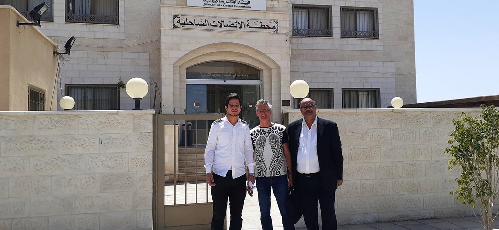 three men in front of an arabic looking official building of very pale cream stone.