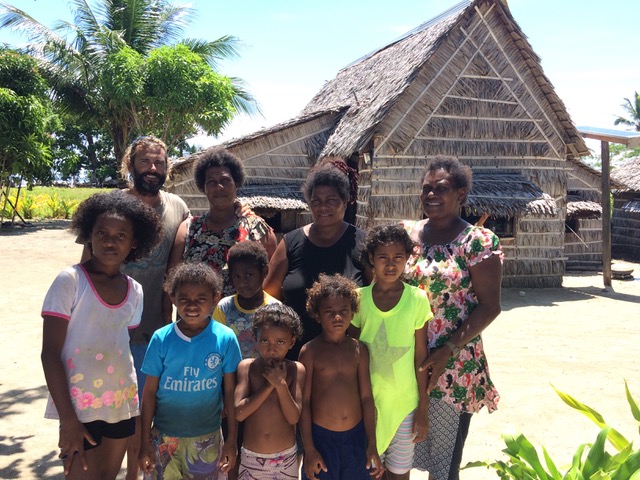 a group of locals women men and children with the skipper standing in front of a traditional house