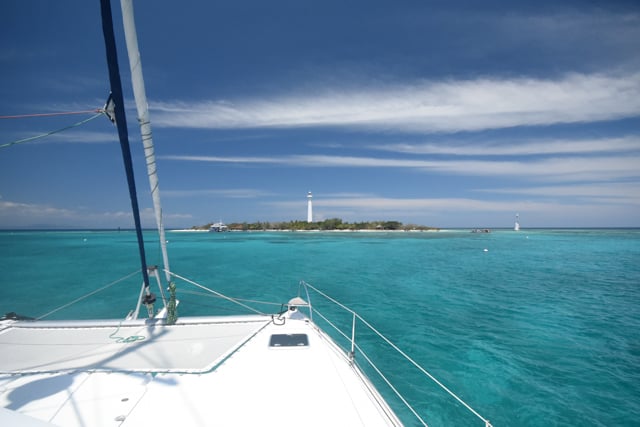 looking towards a lighthouse on an island with the catamarans bow in the foreground.