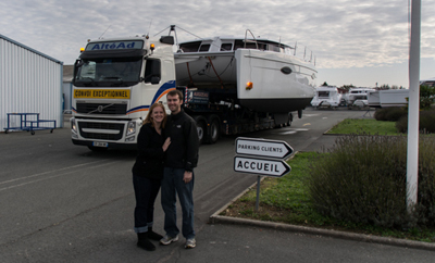 man and woman standing on road in front of catamaran on trailer.