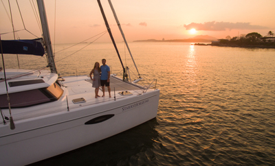 man and woman on bow of catamaran at sunset
