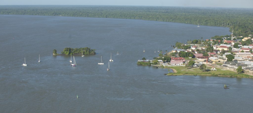 aerial view of an anchorage with a small wooded island on the left and a small settlement on shore to the right