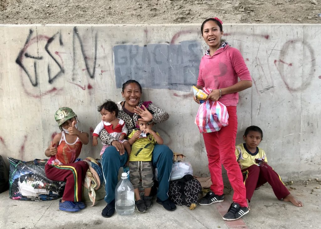 2 local women 2 children and a baby on the sitting ladies lap sat alongside a wall with grafitti