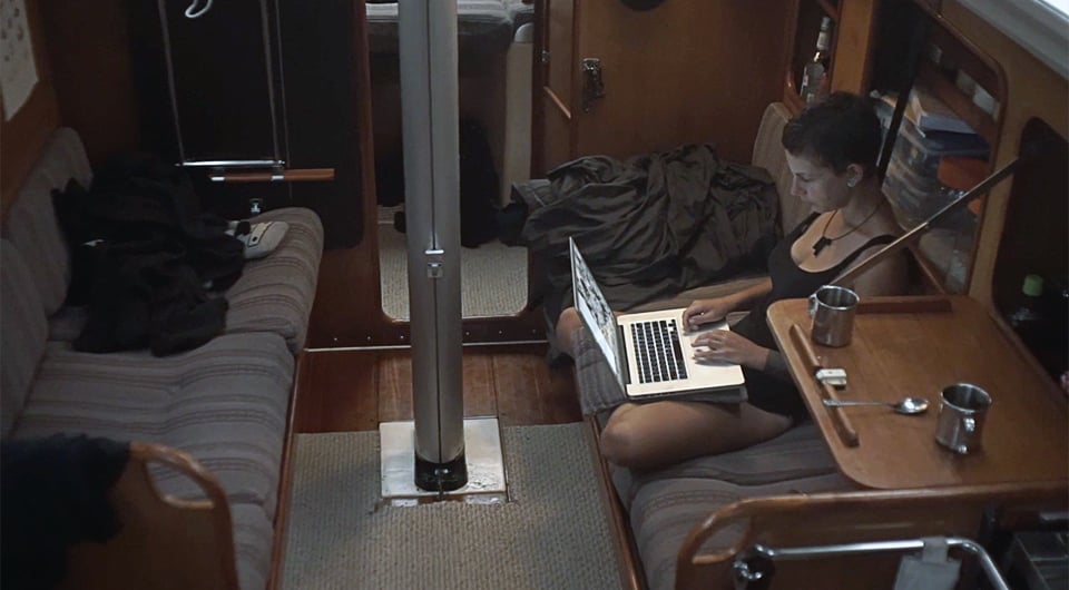 inside of a boat with a girl sitting cross legged on one of the bunks working on a laptop