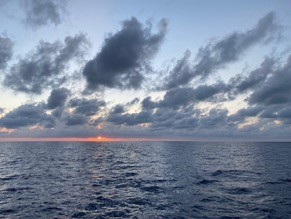 sunrise with a darker sea and darker clouds backed by blue sky