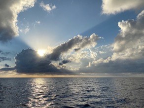 flat grey sea, yellow sunrise and the sun coming out from behind the clouds