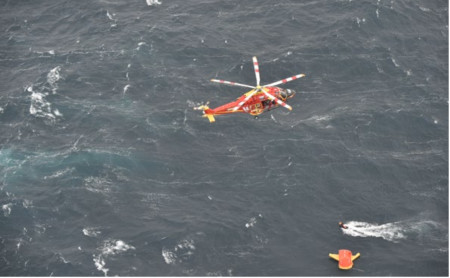 Helicopter hovering over a life raft in rough seas.